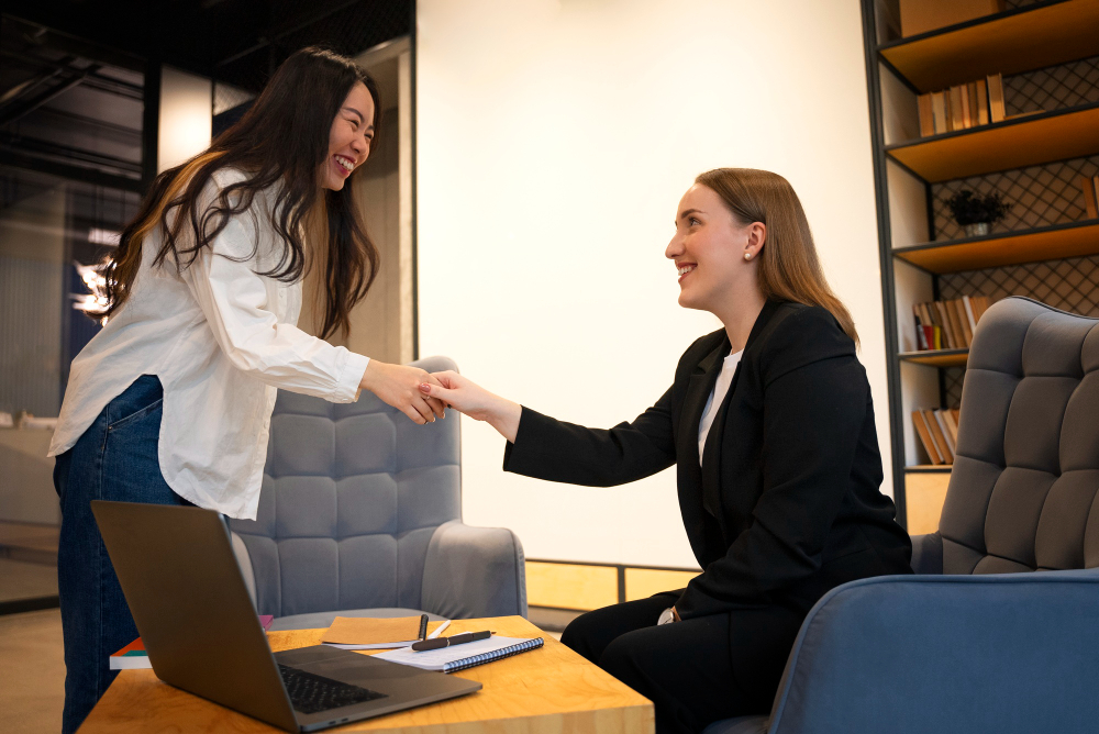 A grinning Asian-American female college junior shakes hands with the American female hiring manager after the internship interview