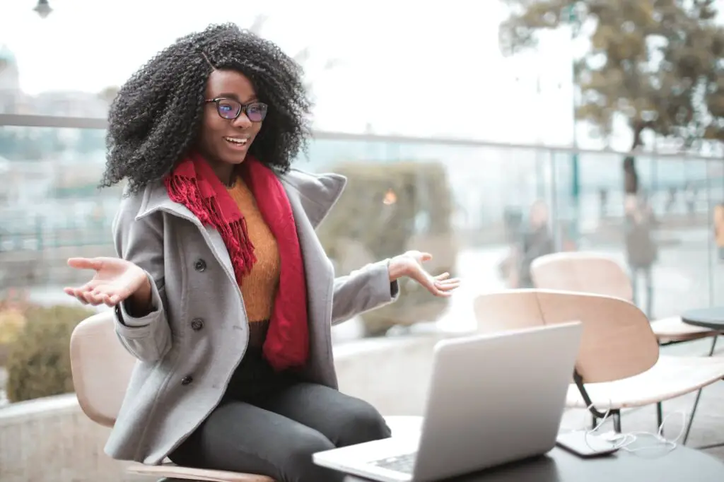 A woman with glasses and a coat sitting on a chair, working on her laptop