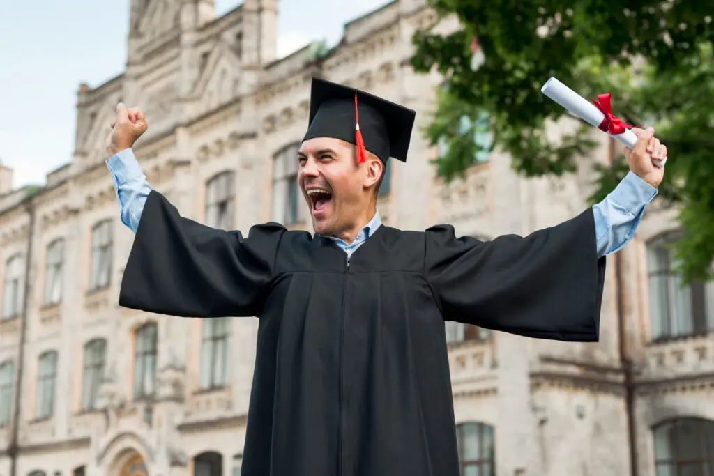 A happy male college graduate wearing his cap and raising his diploma as his student loan repayment grace period starts