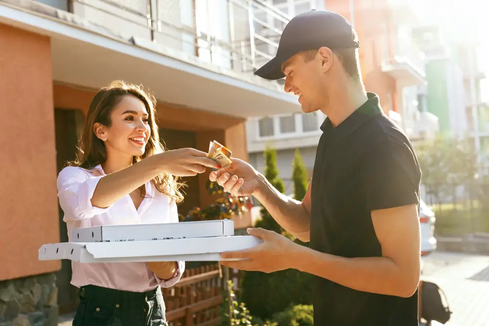A male part-time fast-food worker receiving tips after delivering pizza to a smiling female customer