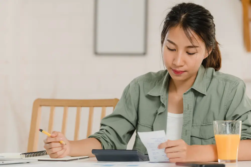 An Asian female college student calculates her debt to prepare her student loan repayment strategy