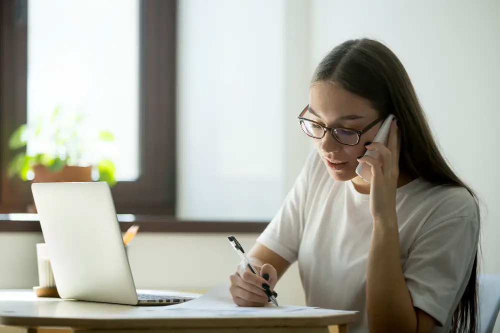 A female international student fills out a bank application form while talking to the bank's customer service on the phone