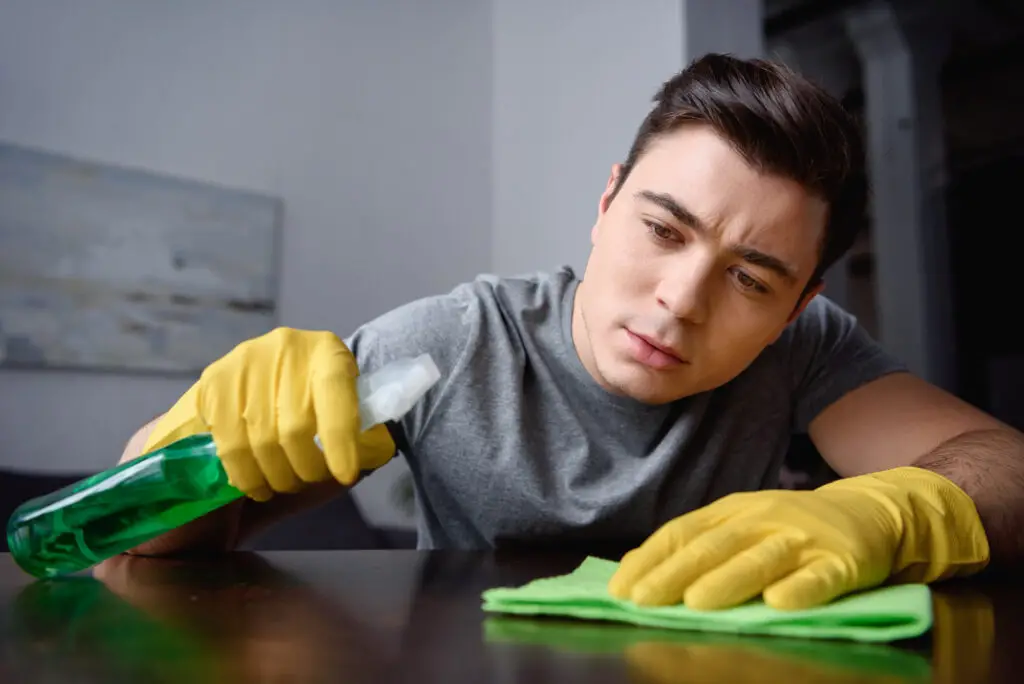 A college student wearing gloves and rubber gloves cleaning a table inside his dorm room