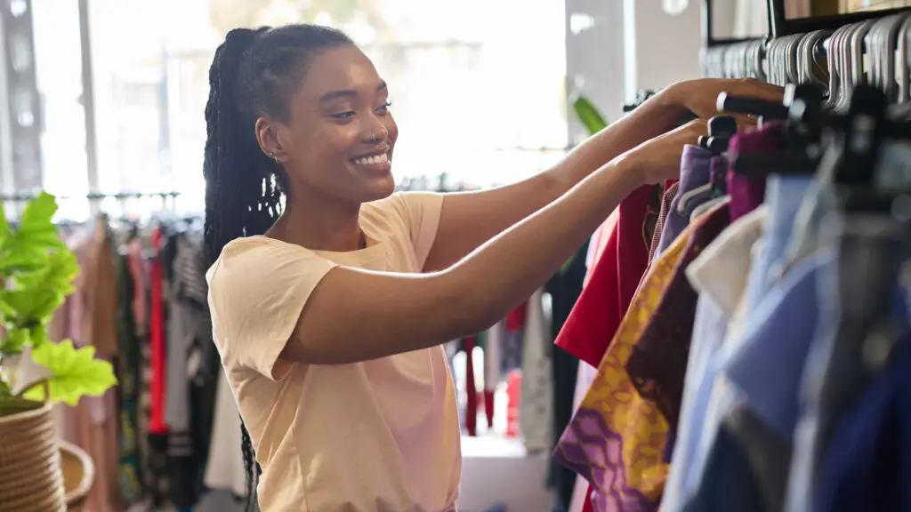 A woman happily browsing clothes on a rack, wearing a bright smile as she selects her college wardrobe essentials