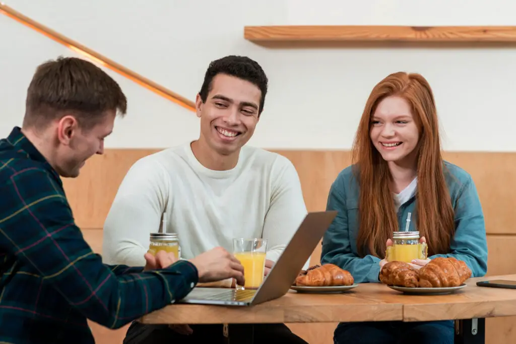 Three college students sitting at a table engrossed in their work on a laptop while eating the best college food