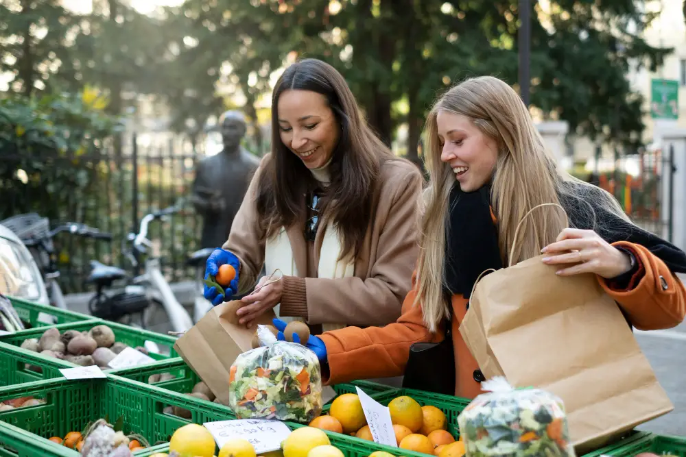 A couple of female college students placing fruits in an eco-bag at a local farmers' market