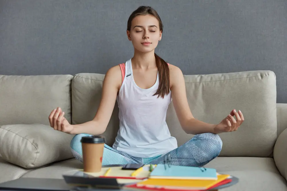 A female student meditates on the sofa during her study break to manage college stress