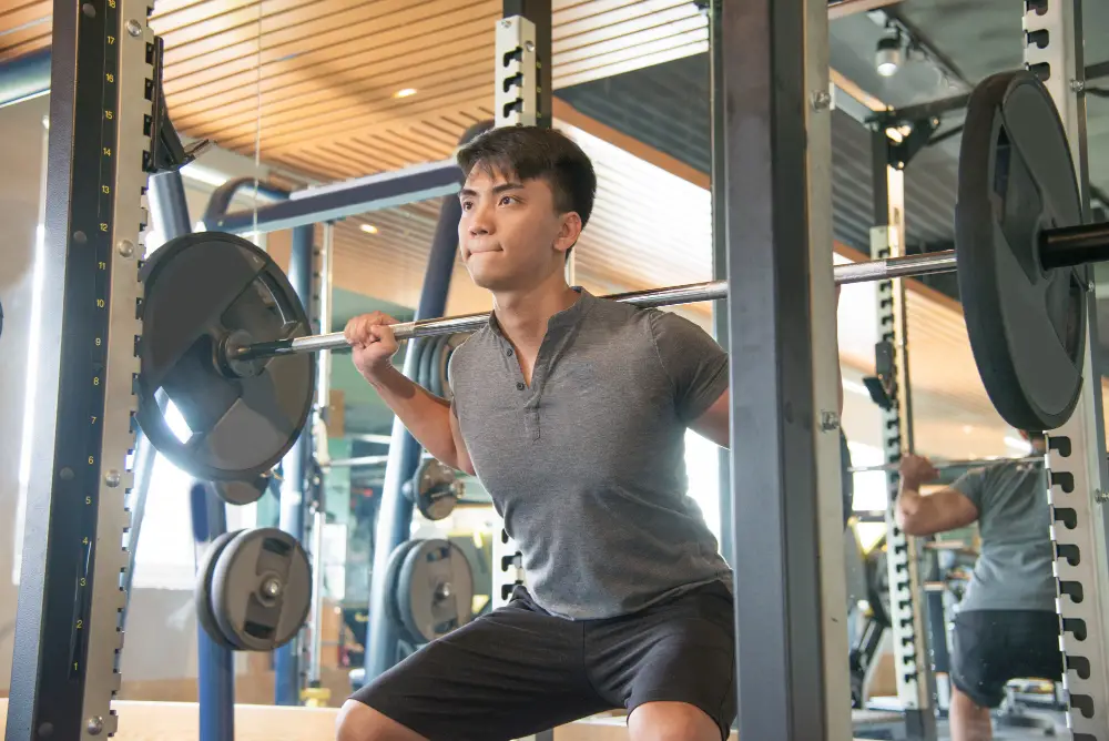 An Asian male college student focuses on his breath while weightlifting in the gym to manage college stress