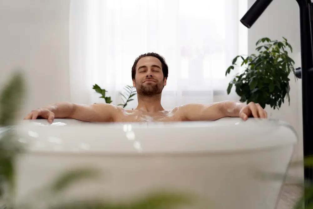 A male college student smiles and closes his eyes as he relaxes in his bubble bath