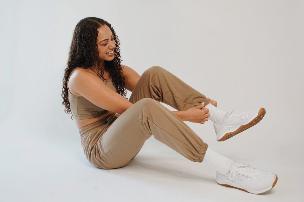 A woman in a tan outfit sitting on the floor wearing sneakers