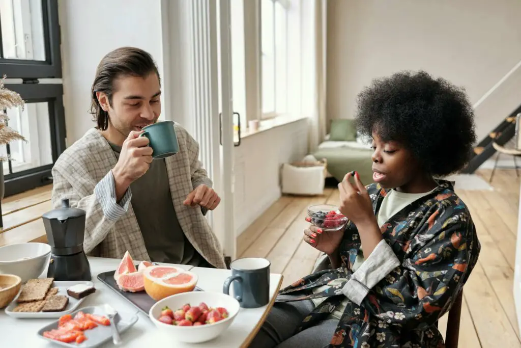 College students sharing a meal in their kitchen table in the dorm room, with plates of food and cups of coffee