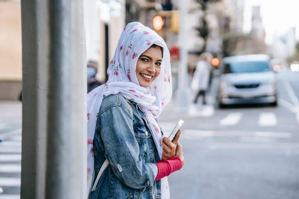 A Muslim college student wearing a hijab and denim jacket on a busy street as part of her college wardrobe essentials