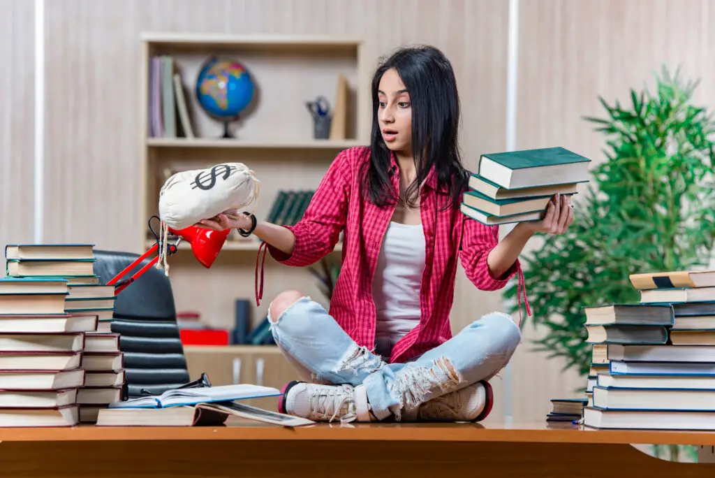 A female college student sitting on a desk surrounded by books and holding a moneybag to signify most expensive colleges
