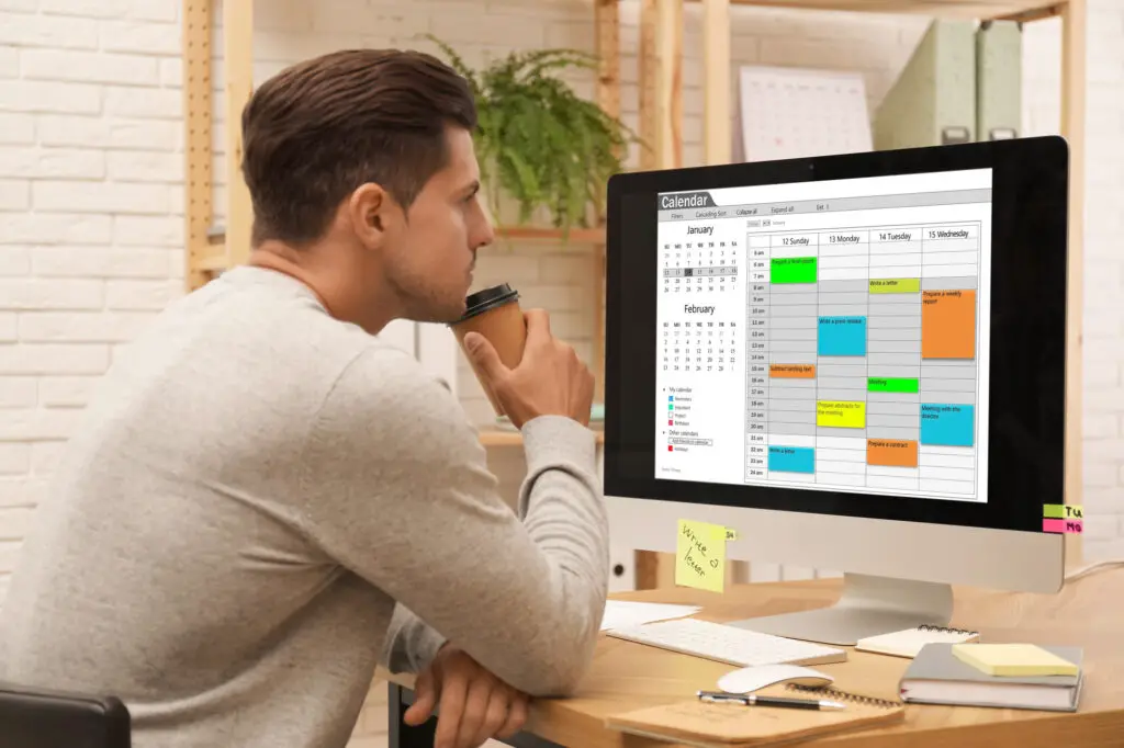 A man sitting at a desk, is focused on his computer screen displaying a calendar