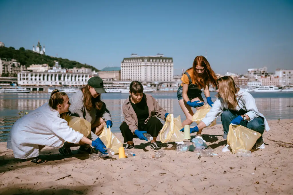 Four young college students pick up trash and debris from the sandy beach, promoting a clean and eco-friendly environment