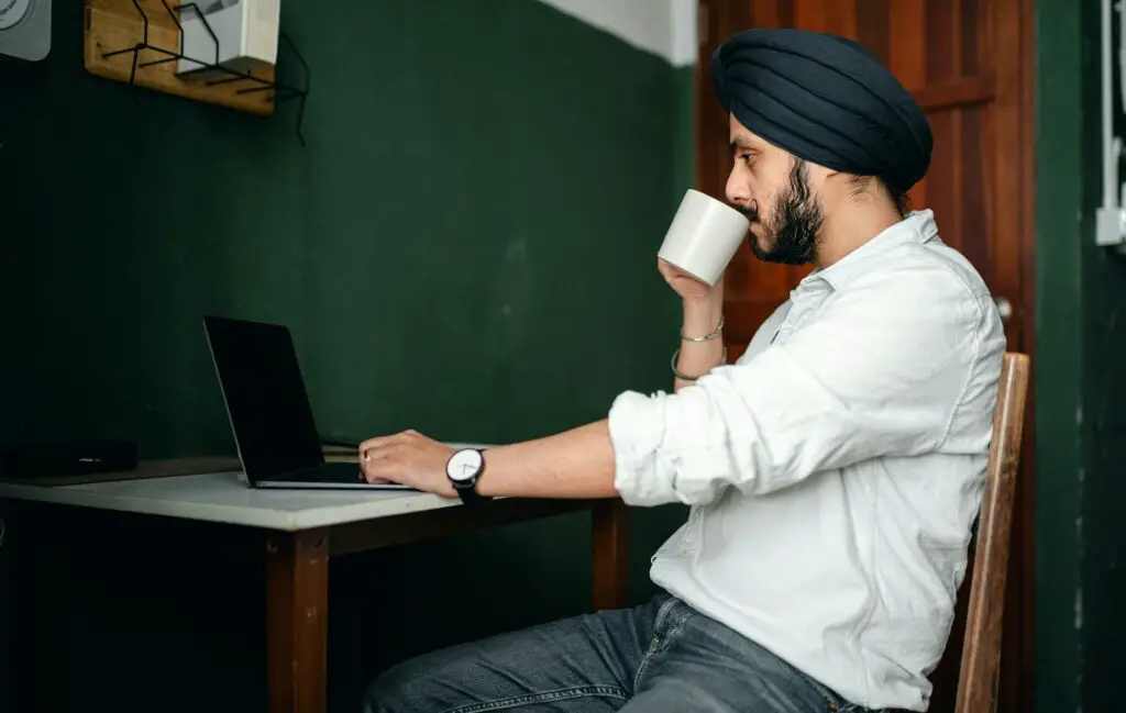 A male college student sitting at a desk drinking from a cup while studying