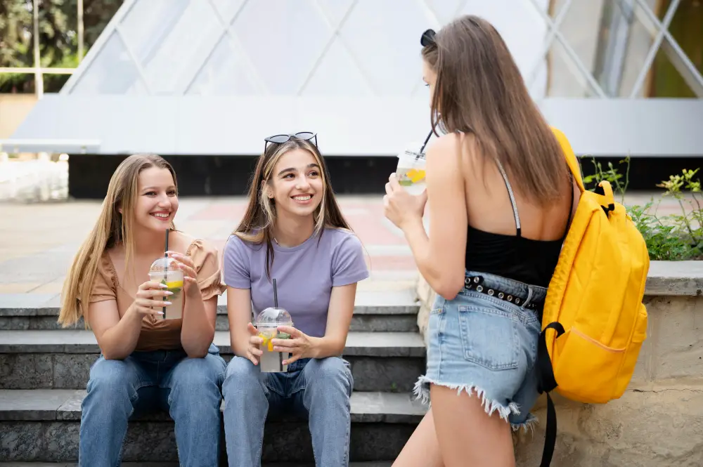 Three happy female college students drinking iced lemonade while hanging out on campus steps