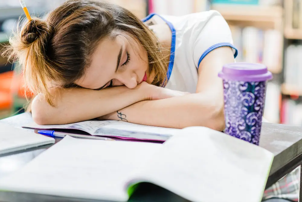 A female college student asleep amid her notes on her desk due to lack of sleep