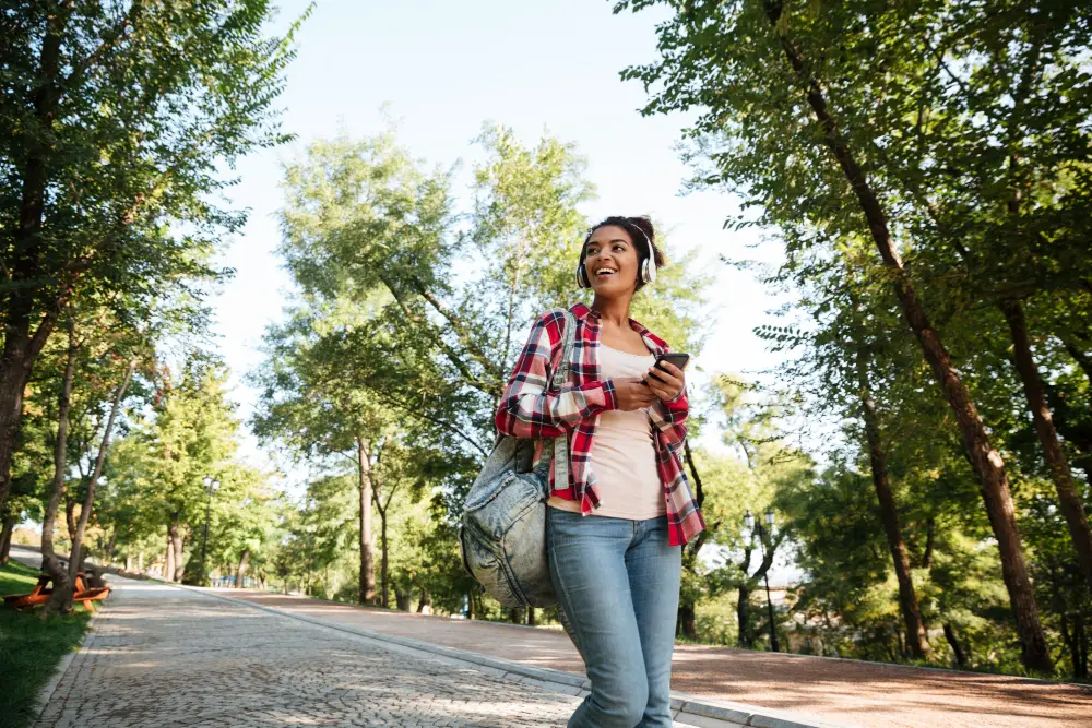 A happy African-American female college student listening to music while strolling on campus grounds to boost good mood