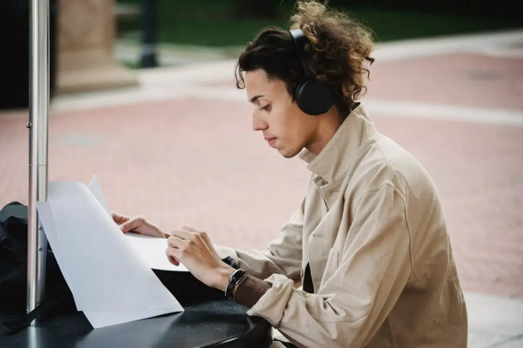 A male college student sitting at a table, wearing headphones, with a piece of paper in front of him.