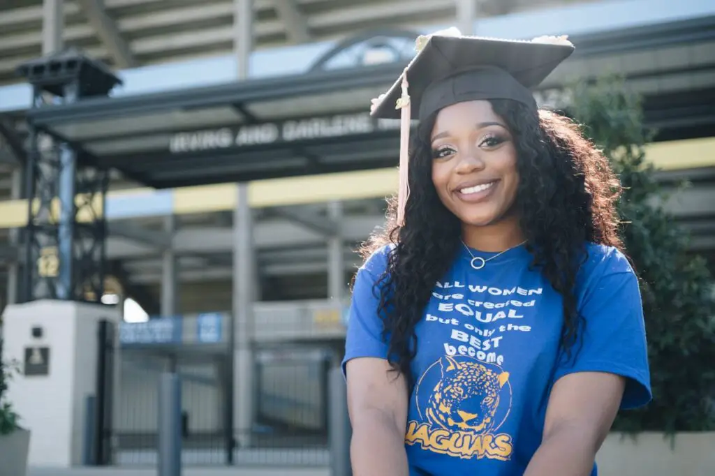 A young woman in a blue graduation cap and gown, smiling proudly at her achievement after completing college graduation requirements