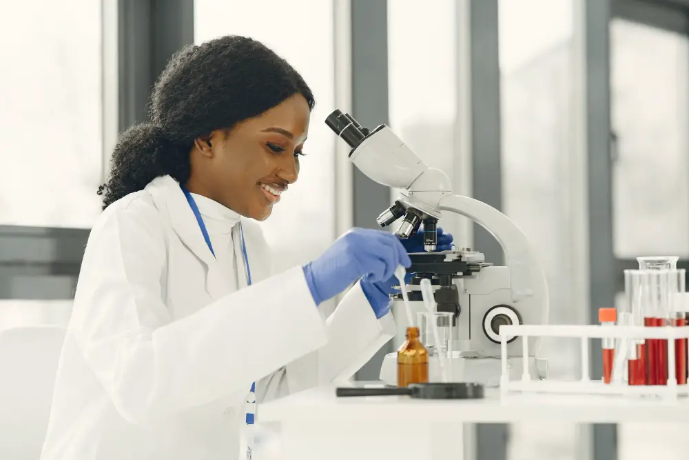 A happy African-American female student checks the slides under a microscope as part of her research program responsibilities