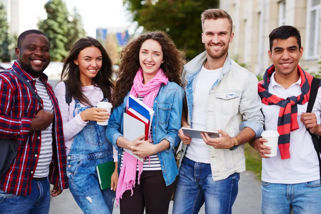 A group of smiling college students wearing comfortable clothes and proudly displaying their books