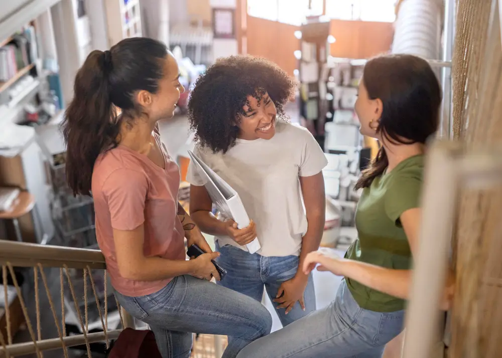 Three sorority girls happily discuss plans after finals exams in the library